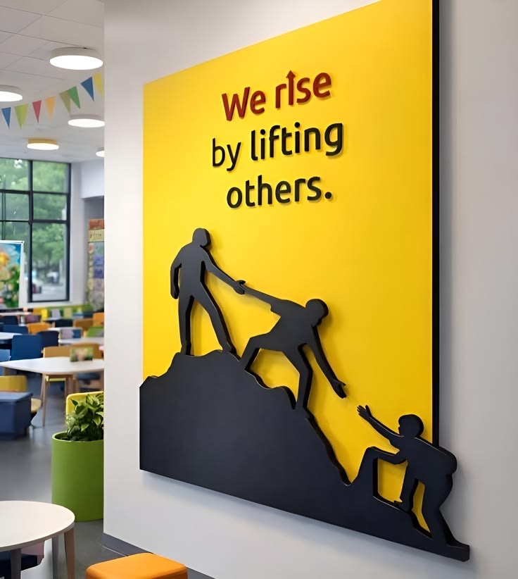 Wall art reading 'We rise by lifting others' in an open collaborative workspace